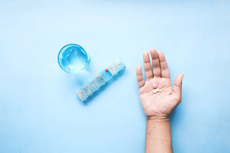 someone's hand holding some medications, along with their pill organizer