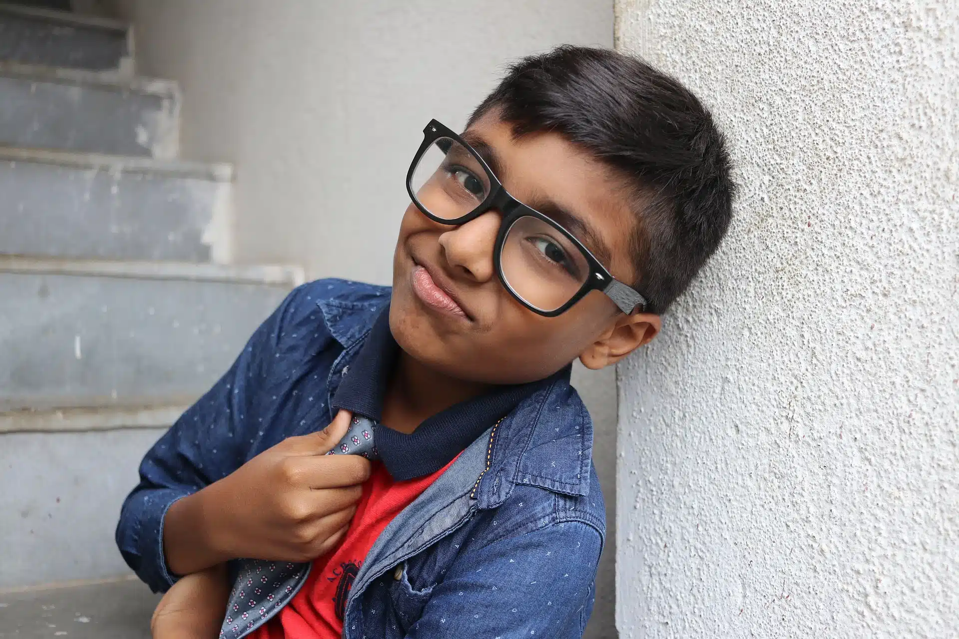 a boy with glasses and a blue t shirt on, smirking at the camera