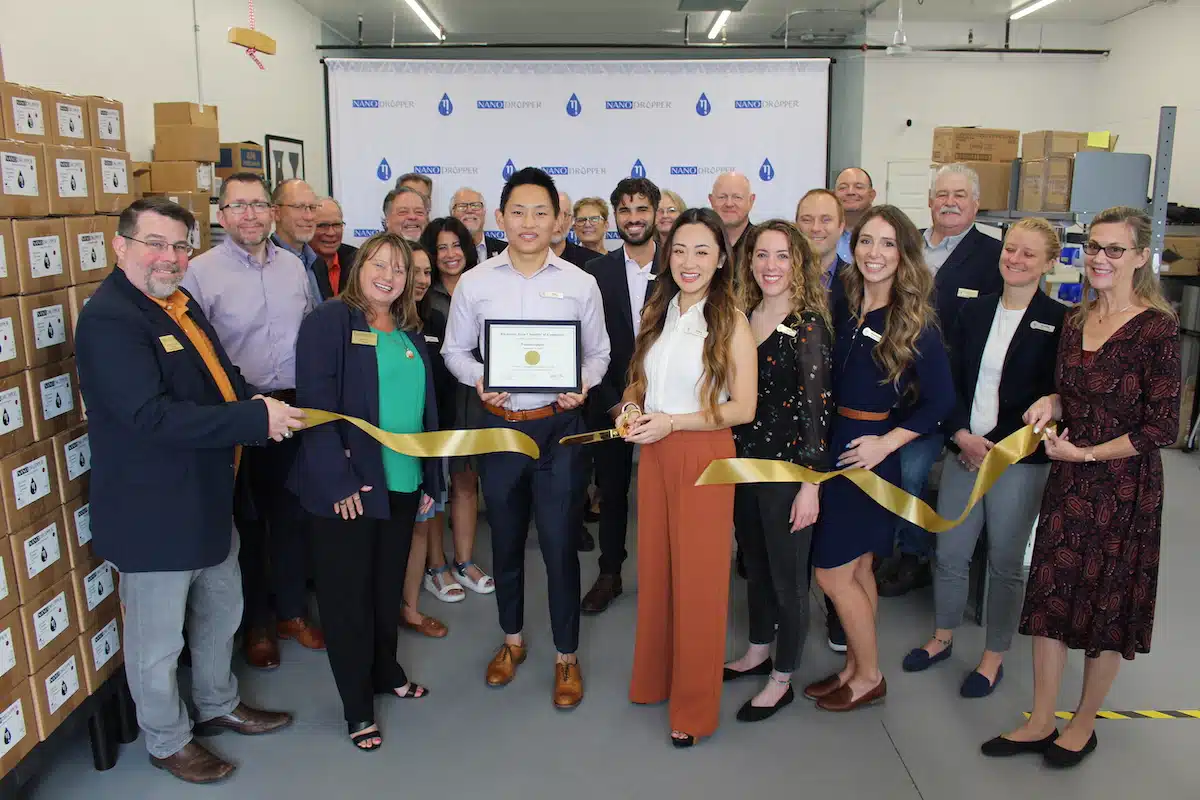 a group of people cutting a golden ribbon at the nanodropper office